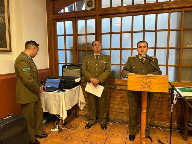 Un oficial habla desde el atril, junto a dos carabineros